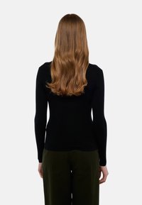 Top noir à manches longues côtelé avec une silhouette ajustée, associé à un pantalon large olive, présentant une texture lisse et un design simple.