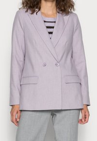 Dvojřadý levandulový blazer s výstřihy, dvěma předními kapsami a dvěma shodnými knoflíky. Nosený přes pruhované tričko a šedé kalhoty.