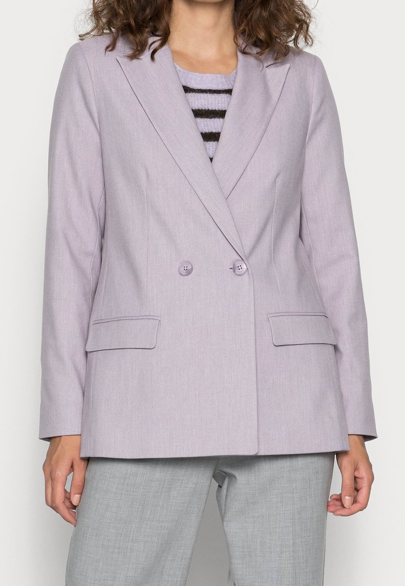 Dvojřadý levandulový blazer s výstřihy, dvěma předními kapsami a dvěma shodnými knoflíky. Nosený přes pruhované tričko a šedé kalhoty.