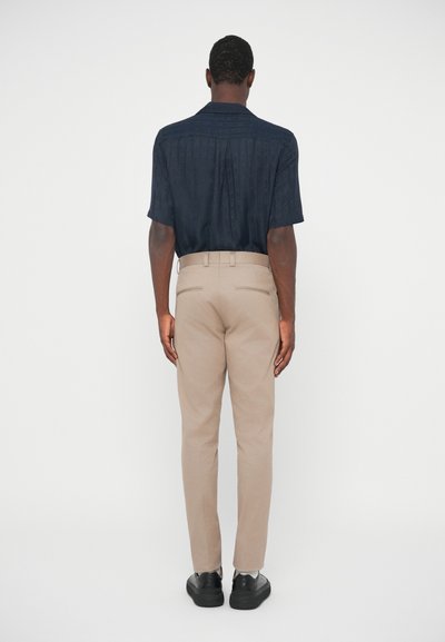 Ναυτικό πουκάμισο κοντό μανίκι με υφή, σε συνδυασμό με ανοιχτό μπεζ παντελόνι και μαύρα παπούτσια, απεικονισμένο από πίσω.