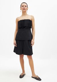 Czarny top bez ramiączek z plisowanymi detalami, w połączeniu z luźnymi czarnymi szortami, eksponującymi gładką fakturę i minimalistyczny design.