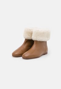 Bottines en cuir marron avec un revers en fourrure crème, présentant un bout arrondi et un design minimaliste, sur une semelle plate.