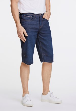 Shorts en denim bleu foncé, avec une coupe droite, un design à cinq poches et des coutures contrastées, associés à des baskets blanches.