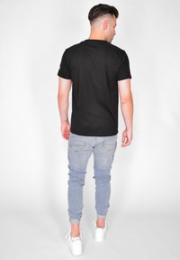 Svart t-shirt med kort ärm och rund halsringning, kombinerad med ljusblå smala jeans och vita sneakers. Minimalistisk design utan mönster.