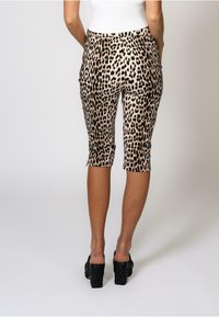 Beige og svart leopardmønstrede capribukser med en tettsittende design, med elastisk midjebånd og sidelommer, avkortet ved midten av leggen.
