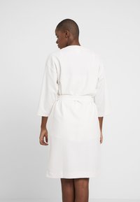 Witte waffle-gepatroneerde badjas met een riem, 3/4 mouwen en een rechte snit. Geweven stof, knielange ontwerp en een ontspannen pasvorm.