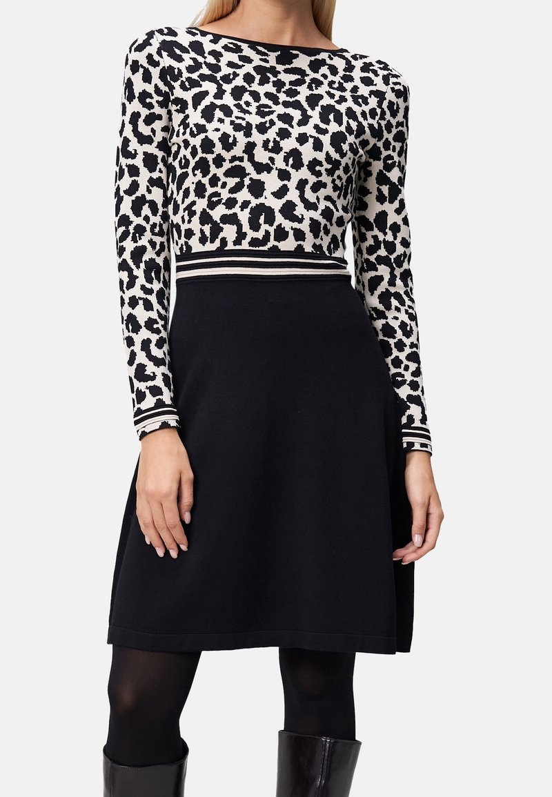 Femme portant une jupe noire et un haut à manches longues avec imprimé léopard noir et blanc, ceinture et poignets rayés.