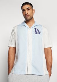 Kurzarmhemd mit Knopfleiste, das hellblaue und weiße Paneele zeigt, mit einem marineblauen "LA"-Logo auf der Brust und einem klassischen Kragendesign.