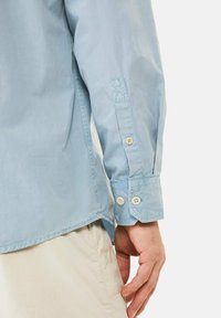 Lichtblauw langemouwen shirt gemaakt van gladde stof, met een manchet met knoopsluiting en contrasterende stikseldetails.