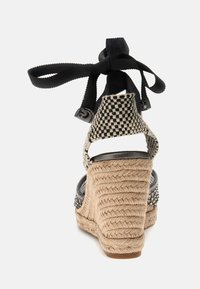 Wedge-sandaal met een geweven jute zool, zwart-witte geblokte bovenkant en een zwarte band om de enkel voor aanpassing.