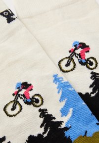 Close-up of cream socks with colorful knit design of cyclists jumping over black and blue trees.