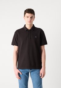 Svart polo skjorte laget av bomull med avslappet passform, med en tre-knappslukking og en liten logo-patch på venstre bryst.