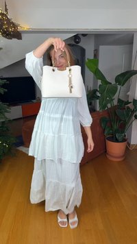 Sac à main blanc avec ferrures dorées et un charm décoratif. Le sac est structuré avec une texture lisse et possède deux poignées supérieures.