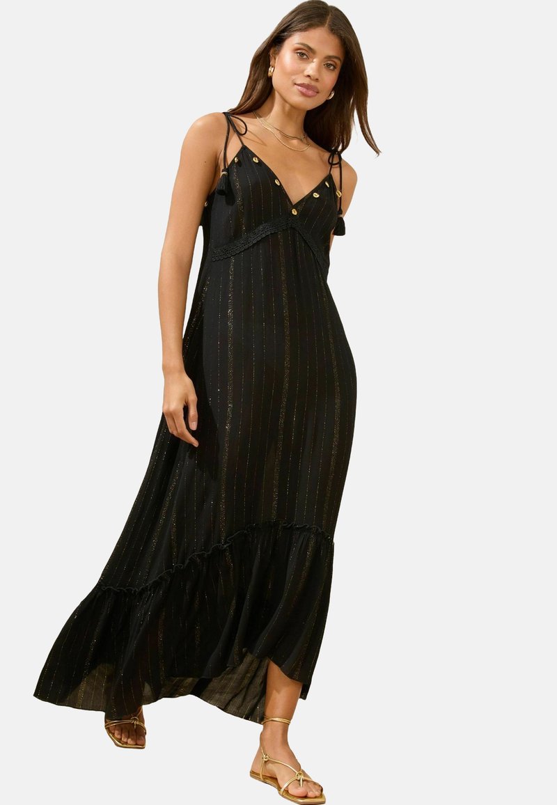 Zwarte maxi-jurk met gouden verticale strepen, kantdetail rond de taille, verstelbare straps en een gerimpelde zoom. Model draagt gouden sandalen.