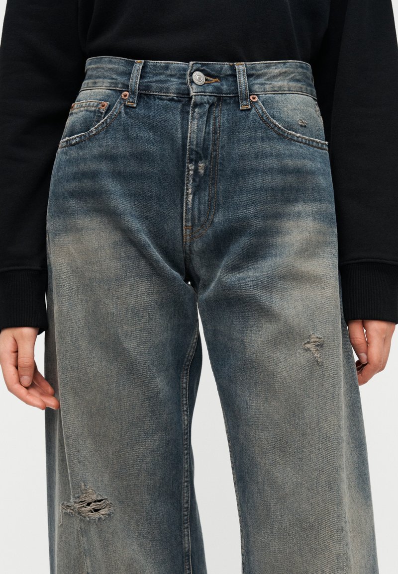 Jean bleu taille haute à jambes larges en denim. Caractérisé par des effets froissés, des accents usés et une fermeture par bouton à la taille.
