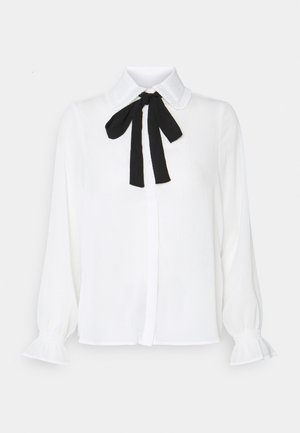 Witte blouse met lange mouwen, gerimpelde manchetten, een geplooide kraag en een zwarte stoffen strik gestrikt rond de hals.
