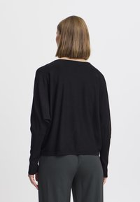 Pull noir à manches longues avec une coupe décontractée, col rond et tissu léger ; présente des épaules tombantes et un ourlet discret.