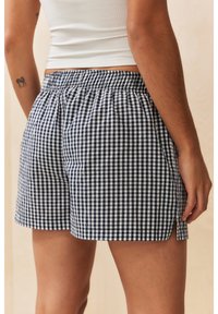 Shorts à carreaux bleu marine et blanc avec une taille élastique, dotés d'une fente latérale pour faciliter les mouvements et d'un tissu en coton léger.