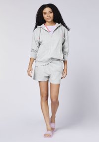 Grey zip-up hoodie with pink accents, paired with matching grey shorts. Model wears purple slide sandals with a graphic design.