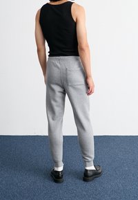 Šedé tepláky s volnějším střihem, elastickým pasem a zadní kapsou. Doplňují je černý top a černé boty.