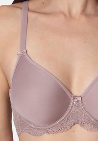 Zart mauve-farbener BH mit glatten Schalen, Spitzenbesatz am unteren Rand und einer dekorativen Schleife am Träger. Mit einem kleinen Herzmotiv in der Mitte.