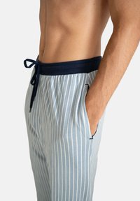 Lichtblauwe pyjamabroek met strepen, een marineblauwe tailleband met trekkoord, zijzakken en een zachte stoftextuur. Verticale strepen en een eenvoudig ontwerp.