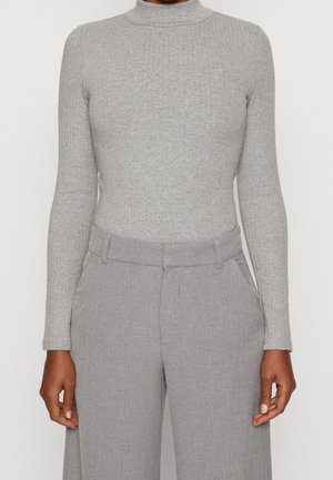 Kobieta ubrana w dopasowany jasnoszary golf z prążkowanego materiału, wpuszczony w szare spodnie z szerokimi nogawkami o wysokim stanie, z bocznymi kieszeniami.