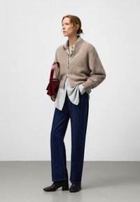 Beige wol cardigan over een gestreepte blauwe shirt, gecombineerd met donkerblauwe jeans en zwarte hoge laarzen. Bordeauhandtas in één hand.