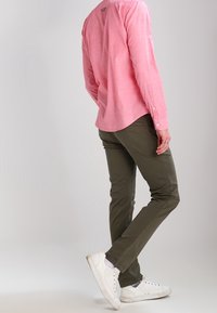 Hellrosa Langarmhemd mit Knopfdetails, kombiniert mit olivgrünen Hosen und weißen Sneakern, die einen lässigen Schnitt und Textur zeigen.