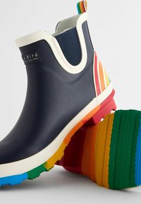Stivale in gomma navy con bordi bianchi e accenti a strisce arcobaleno sul tallone. Suola testurizzata e multicolore con un motivo ondulato.