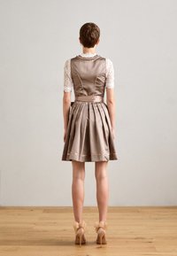 Femme debout, vue de dos, portant une robe taupe à motifs avec des manches en dentelle et des talons nus ornés de grands nœuds.