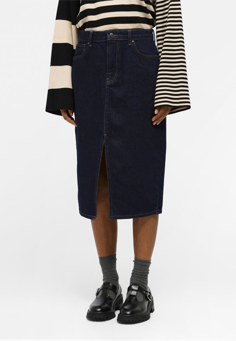 Jupe midi en denim bleu foncé avec une fente à l'avant portée avec des chaussures noires à boucle, des chaussettes grises et un haut rayé noir et blanc à manches longues.