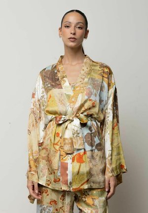 Donna che indossa una giacca kimono patchwork floreale a maniche lunghe con cintura e pantaloni abbinati in morbide tonalità della terra.