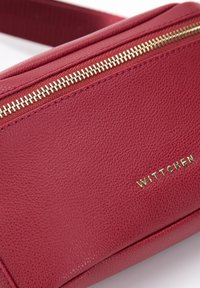 Czerwona, teksturowana skórzana torebka na ramię z złotym zamkiem błyskawicznym i wytłoczonym logo "WITTCHEN" z przodu. Kompaktowy i prostokątny kształt.