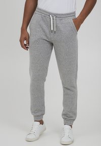 Gray sweatpants made of soft fabric, featuring an elastic waistband with drawstrings, tapered legs, and side pockets. Paired with white sneakers.