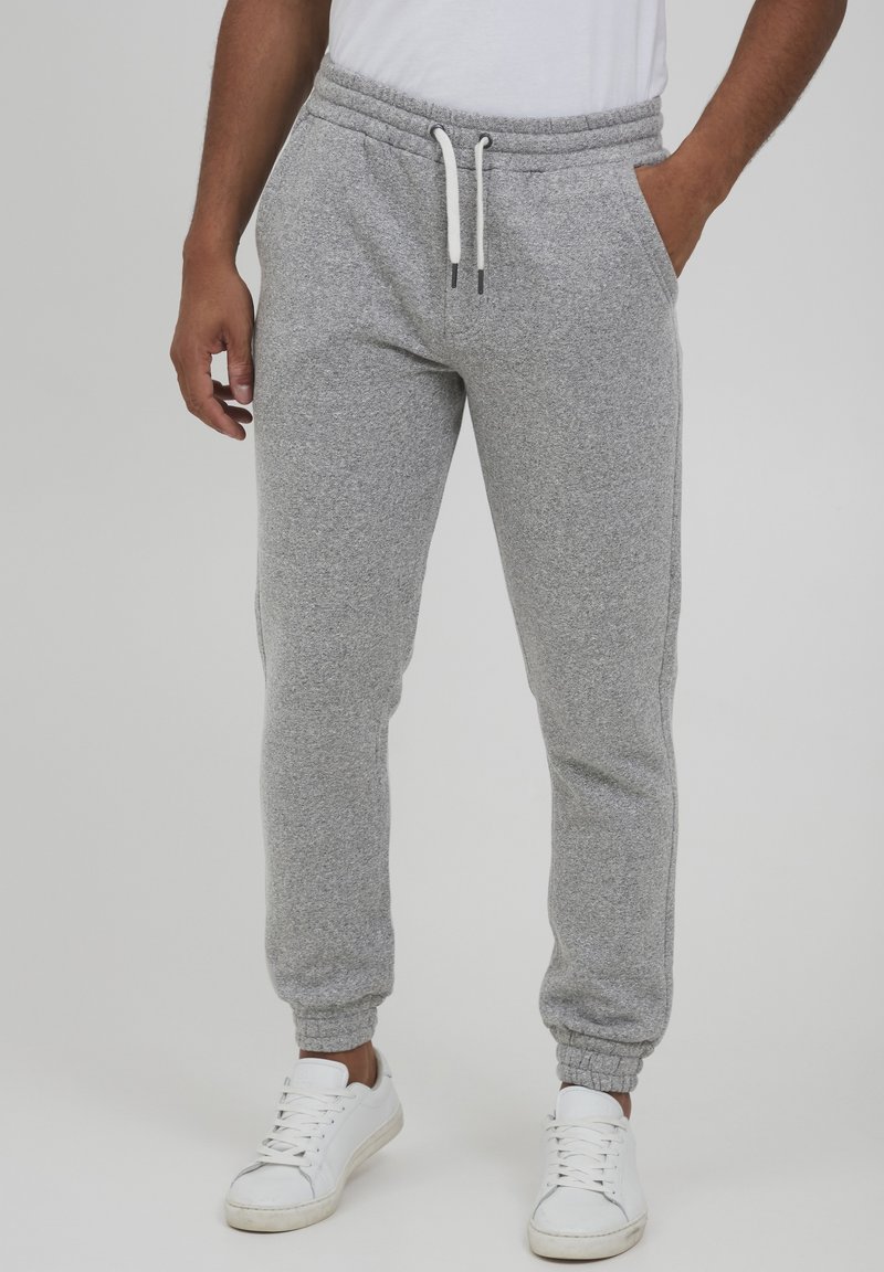 Gray sweatpants made of soft fabric, featuring an elastic waistband with drawstrings, tapered legs, and side pockets. Paired with white sneakers.