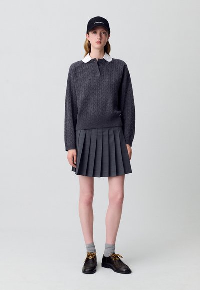 Maglione grigio a maglia grossa con colletto bianco, gonna plissettata grigia, calze grigie e scarpe nere con lacci gialli; berretto nero.