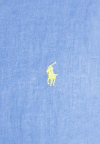 Light blue fabric featured with a small yellow embroidered polo player logo, showing smooth, textured weave.