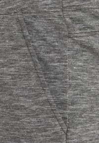 Šedá joggingová tkanina s jemnou melírovanou strukturou, obsahující postranní kapsy a elastický pas pro pohodlí a flexibilitu.