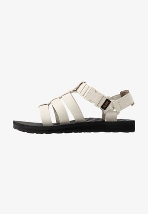 Beige sandal with three fabric straps and a plastic buckle. Features a textured black rubber sole. Flat design for comfort and stability.
