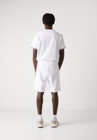 Tenue de sport blanche comprenant un haut à manches courtes avec des bordures noires et un short assorti, design simple et taille élastique.