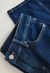 Tamsiai mėlynos džinsinės kelnės tiesiu kirpimu, su kontrastinga oranžine siūle, priekinė kišenė ir metalinė mygtuko detalė.