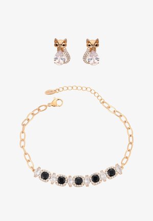 Arany lánc karkötő váltakozó fekete és áttetsző drágakövekkel, arany rókafülbevalókkal párosítva, melyek áttetsző csepp alakú drágaköveket tartanak.