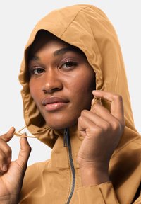 Veste brune, imperméable, avec une fermeture éclair sur le devant et une capuche ajustable. Détail à cordon près du visage, texture lisse et design ajusté.