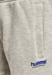Lichtgrijze sweatpants van zacht, gestructureerd materiaal. Voorzien van een zijzak en een blauw "hummel sportswear" logo op de voorkant.