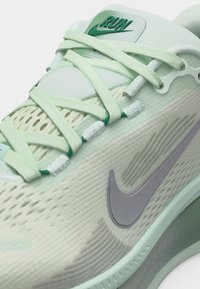 Ανοιχτό πράσινο παπούτσι Nike για τρέξιμο με πλέγμα επάνω μέρος, κορδόνια που διασταυρώνονται και γκρι λογότυπο Nike swoosh στο πλάι.