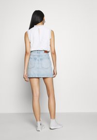 Chemisier en dentelle blanche avec un col à volants, associé à une jupe en denim bleu clair. Les caractéristiques notables comprennent deux poches arrière et une ceinture marron.