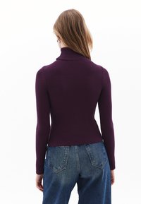 Lila ribbad polotröja med en figurnära design och långa ärmar, i kombination med högmidjade blå denimjeans.