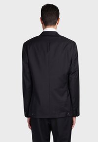 Giacca nera dal taglio strutturato, con tessuto liscio, spacco singolo sul retro e maniche con bottoni e cuciture decorative.