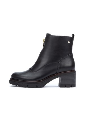 Bottine en cuir noir avec un talon épais, fermeture éclair, accents subtils et une semelle robuste pour une meilleure adhérence. Texture lisse et design épuré.